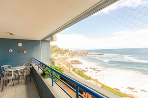 Un balcón con vista al océano, una mesa con sillas y una barandilla.