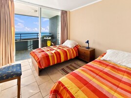 Camera d'albergo con due letti, un comodino, una sedia e vista sul mare.