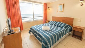 A hotel room with a bed, a desk with a computer, a nightstand, and a window with curtains. - Oceana Suites EuroVista (Vina del Mar)