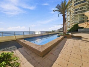 Una piscina con vistas al mar, una palmera y un edificio al fondo.
