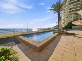 Una piscina con vistas al mar, una palmera y un edificio al fondo.
