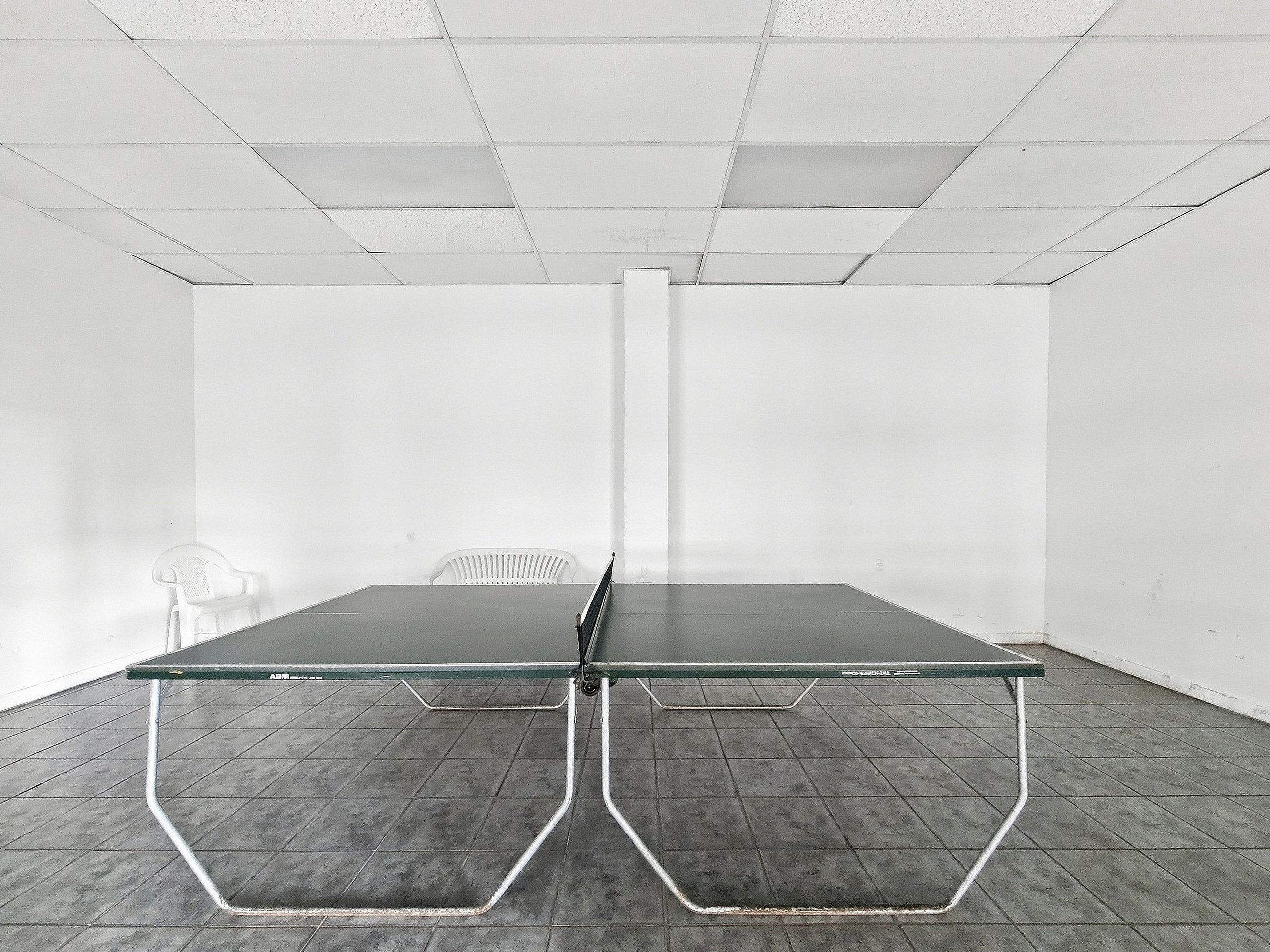 Una habitación con mesa de ping pong, una silla blanca y una pared blanca.