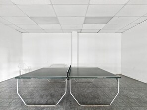 Una habitación con mesa de ping pong, una silla blanca y una pared blanca.