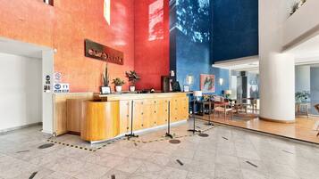A hotel reception area with a wooden reception desk, potted plants, and a large wall mural.