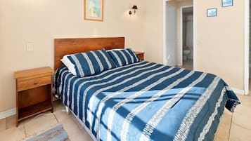 A bedroom with a wooden headboard, a bed with a blue and white striped bedspread, two bedside tables, a nightstand, a door, and a wall-mounted light fixture.