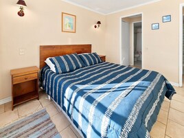 Una camera da letto con testiera in legno, un letto con copriletto a righe blu e bianche, due comodini, una abat-jour e un lampadario a parete.