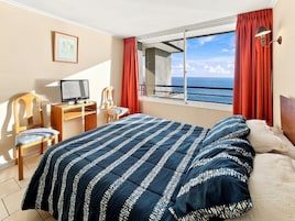 Habitación de hotel con una cama, un escritorio con ordenador, una silla y ventana con vista al mar.
