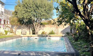 A rectangular swimming pool with a wooden deck, surrounded by greenery and a stone wall. - Appartement Larenceto II vue mer Avec Piscine (Biguglia)