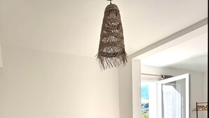 A bedroom with a bed, a woven light fixture, a small bedside table, and a view through a glass door.
