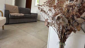 A modern living room with a grey sofa, a glass vase with dried flowers, and a white cabinet.