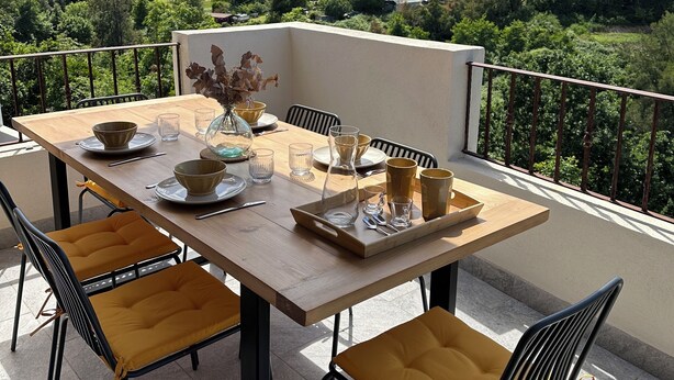 A dining table set outdoors with chairs, a vase, and a scenic mountain view in the background.