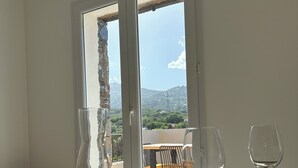 A dining table set with plates, glasses, and cutlery, with a view of a balcony and mountains in the background.