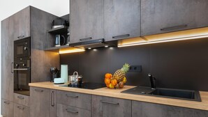 Une cuisine moderne avec des meubles de couleur sombre, un évier en acier inoxydable et un plan de travail agrémenté d’un panier de fruits.