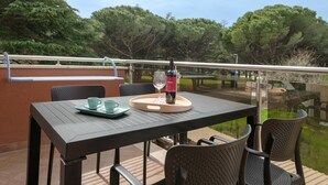 Une table avec un plateau, deux tasses et une bouteille, placée sur un balcon donnant sur un plan d’eau et des arbres.