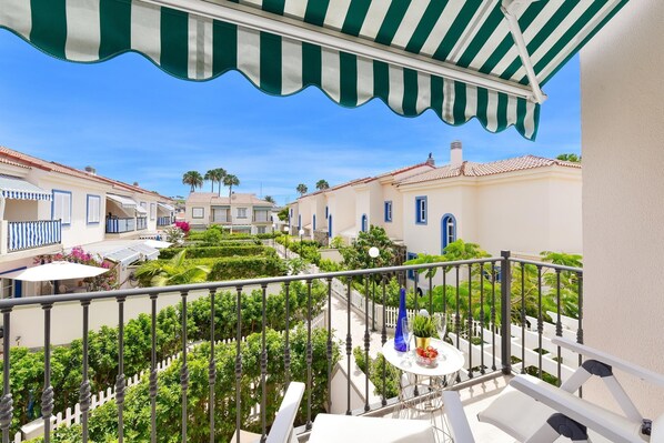 A balcony with a striped awning, white railing, and a table with a vase and a plate of fruit. - Marina Port 15 by VillaGranCanaria (Pasito Blanco)