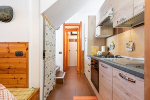 Eine schmale Küche mit Holzschränken, einem Herd und einer gefliesten Spritzschutzwand.