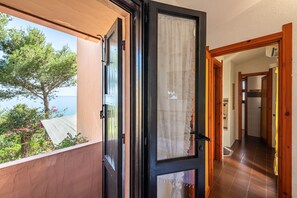 Eine offene Tür, die zu einem Balkon mit Blick auf Bäume und das Meer führt.