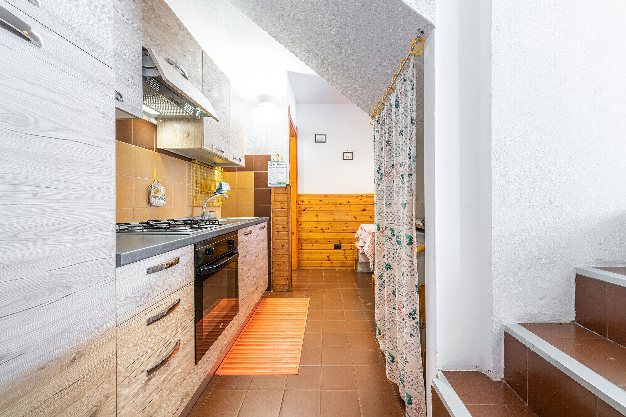 A narrow kitchen with wooden cabinets, a gas stove, and a tiled backsplash.