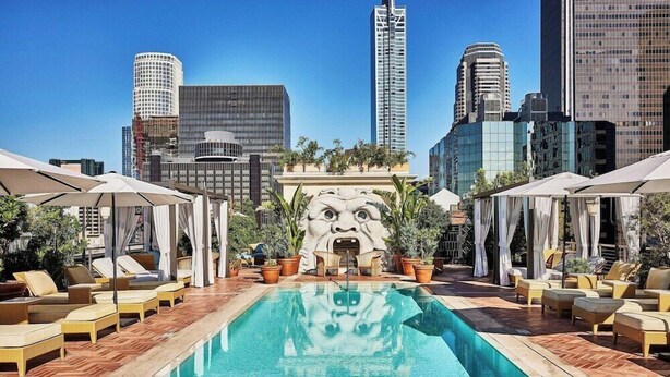 A rooftop pool with lounge chairs and umbrellas, surrounded by city buildings. - Hotel Per La (Los Angeles)