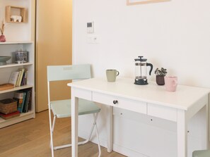 Una mesa blanca con una silla verde, una cafetera y dos tazas.