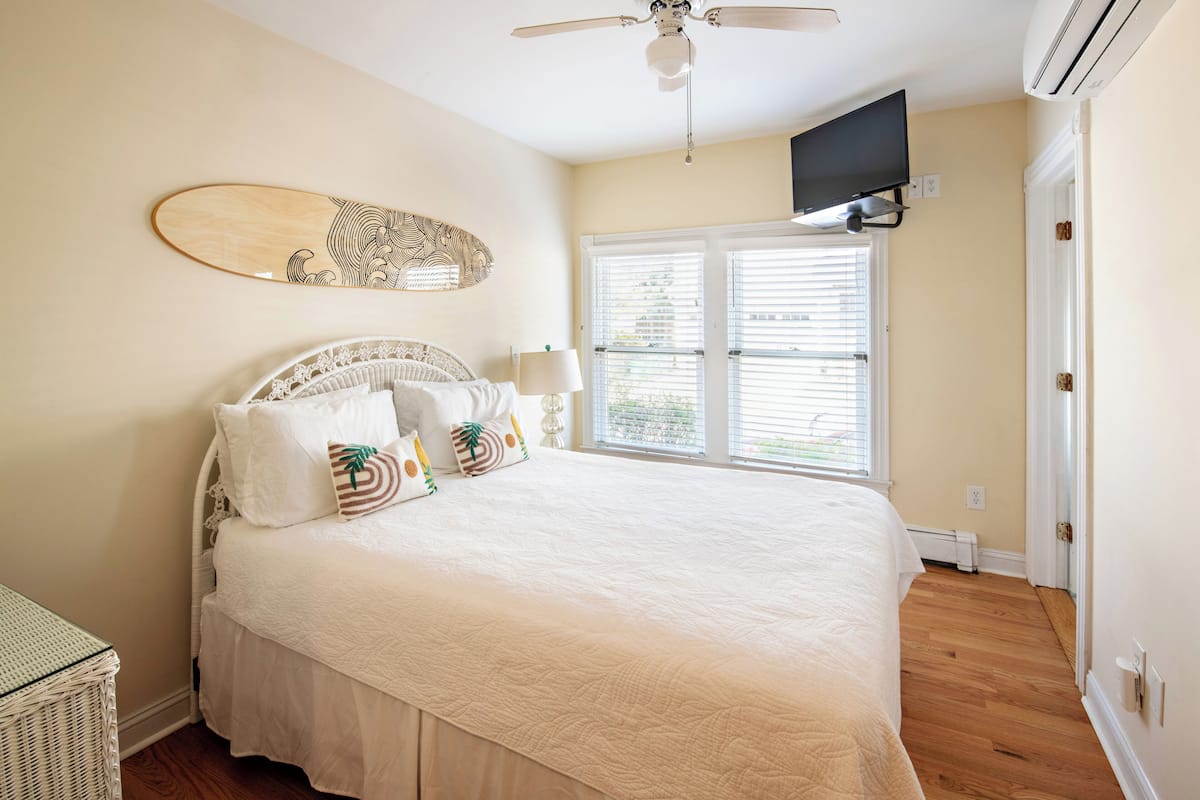 A bedroom with a bed, a ceiling fan, a mounted TV, and a window with blinds.