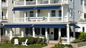 A two-story hotel with a balcony on the second floor, a covered front porch, and a sign indicating availability. - Shawmont Hotel  (Ocean Grove)