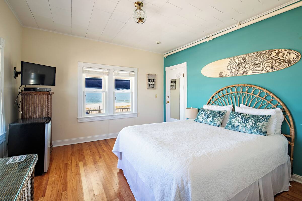 A bedroom with a bed, a television, a window with a view, and a surfboard on the wall.