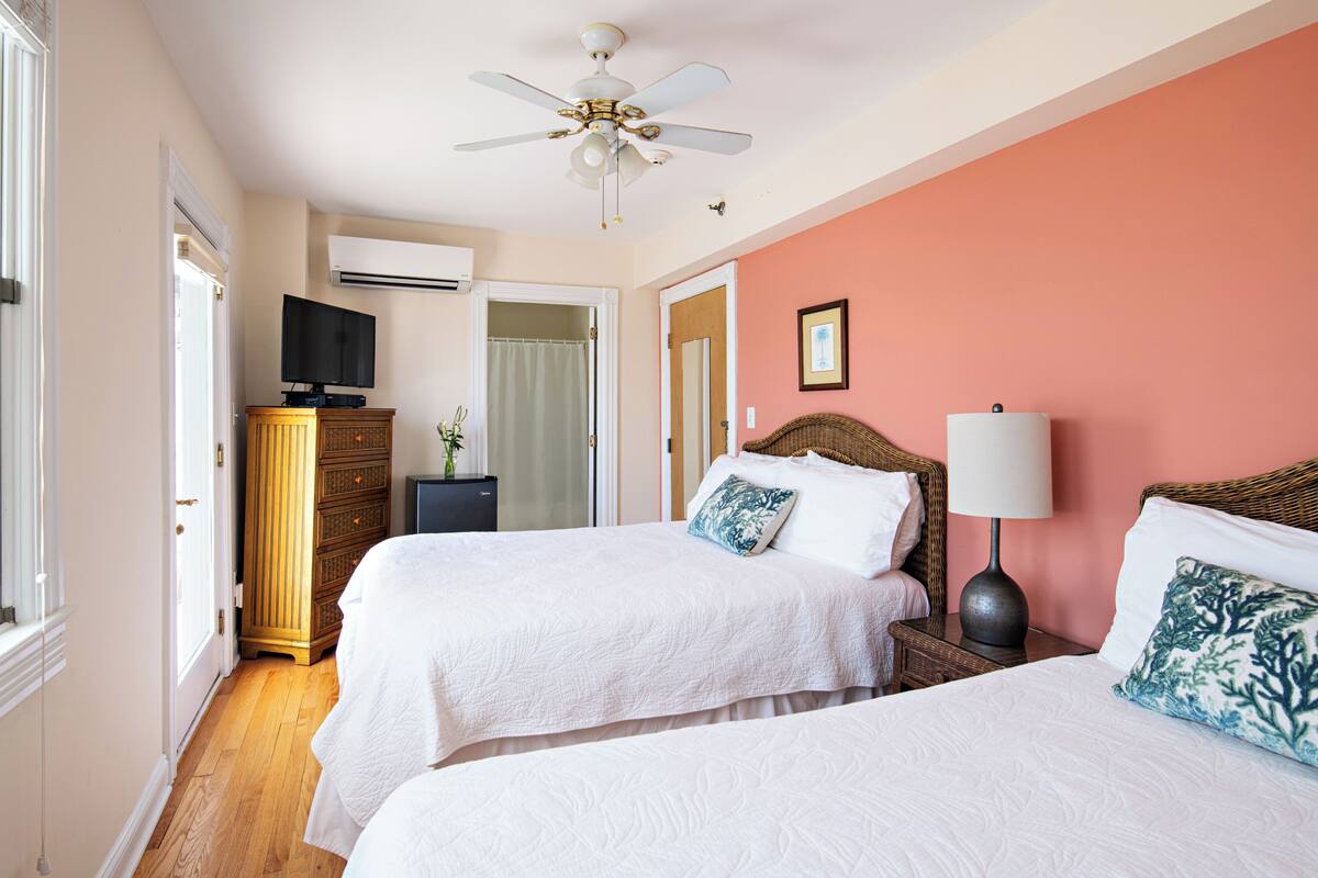 A hotel room with two beds, a ceiling fan, a television, and a dresser.