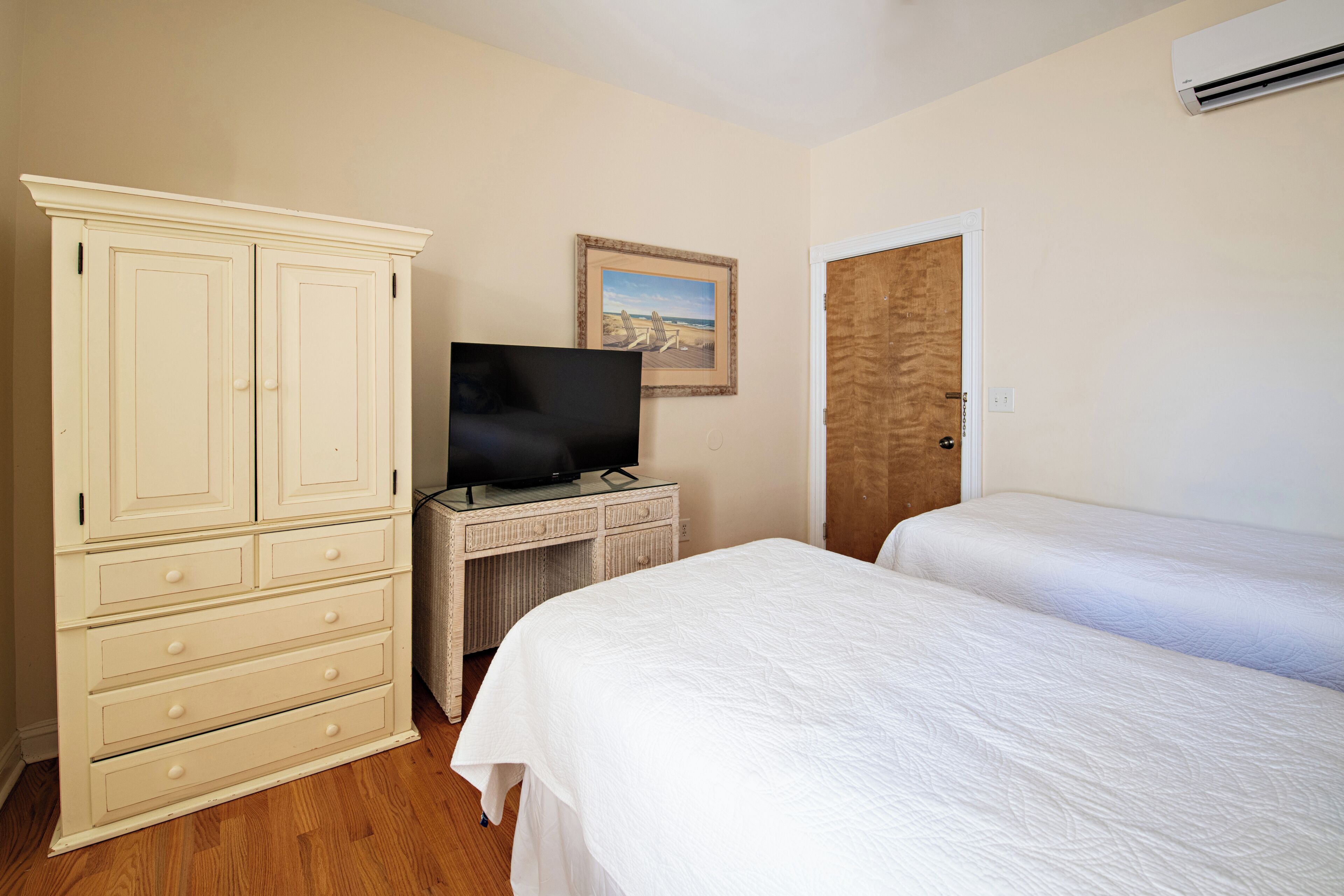 A bedroom with a TV, a dresser, a desk, and two beds.