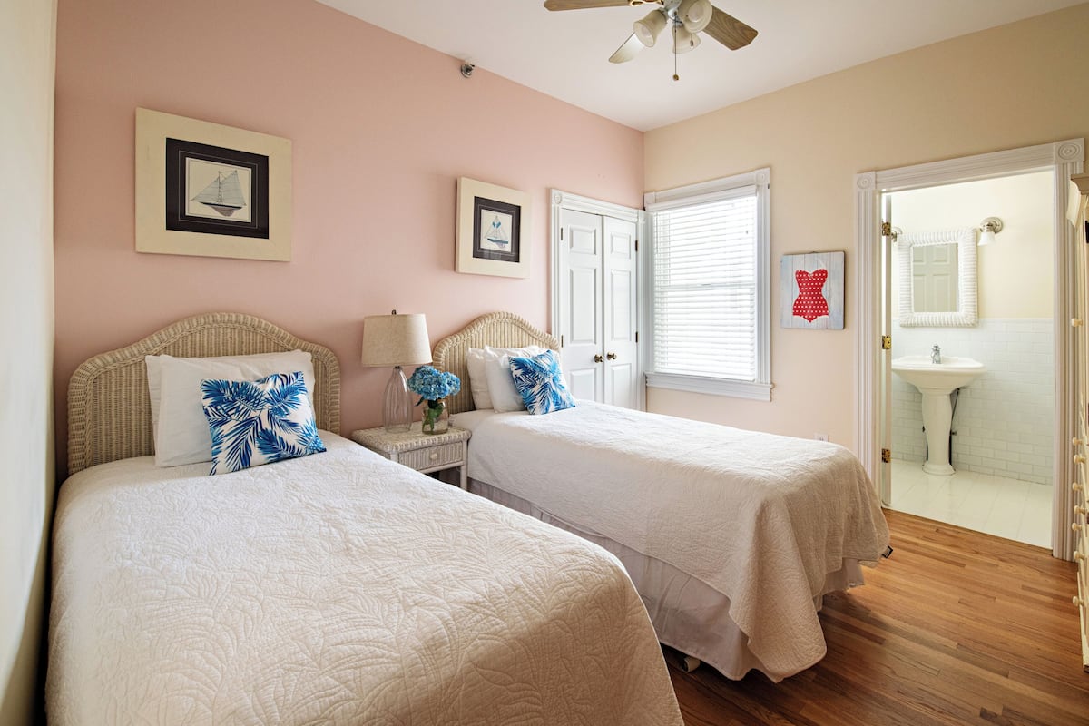 A bedroom with two beds, a nightstand, a ceiling fan, and a bathroom visible through an open door.