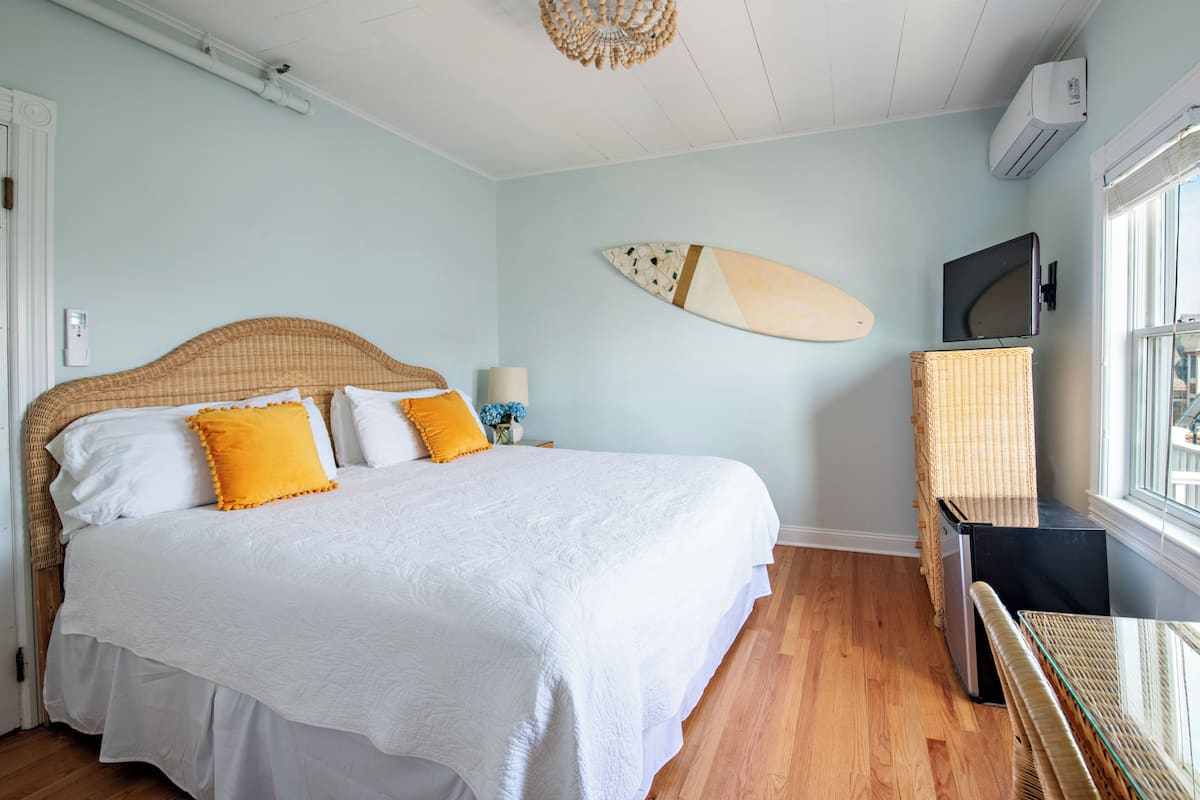 A bedroom with a bed, a television, and a surfboard on the wall.
