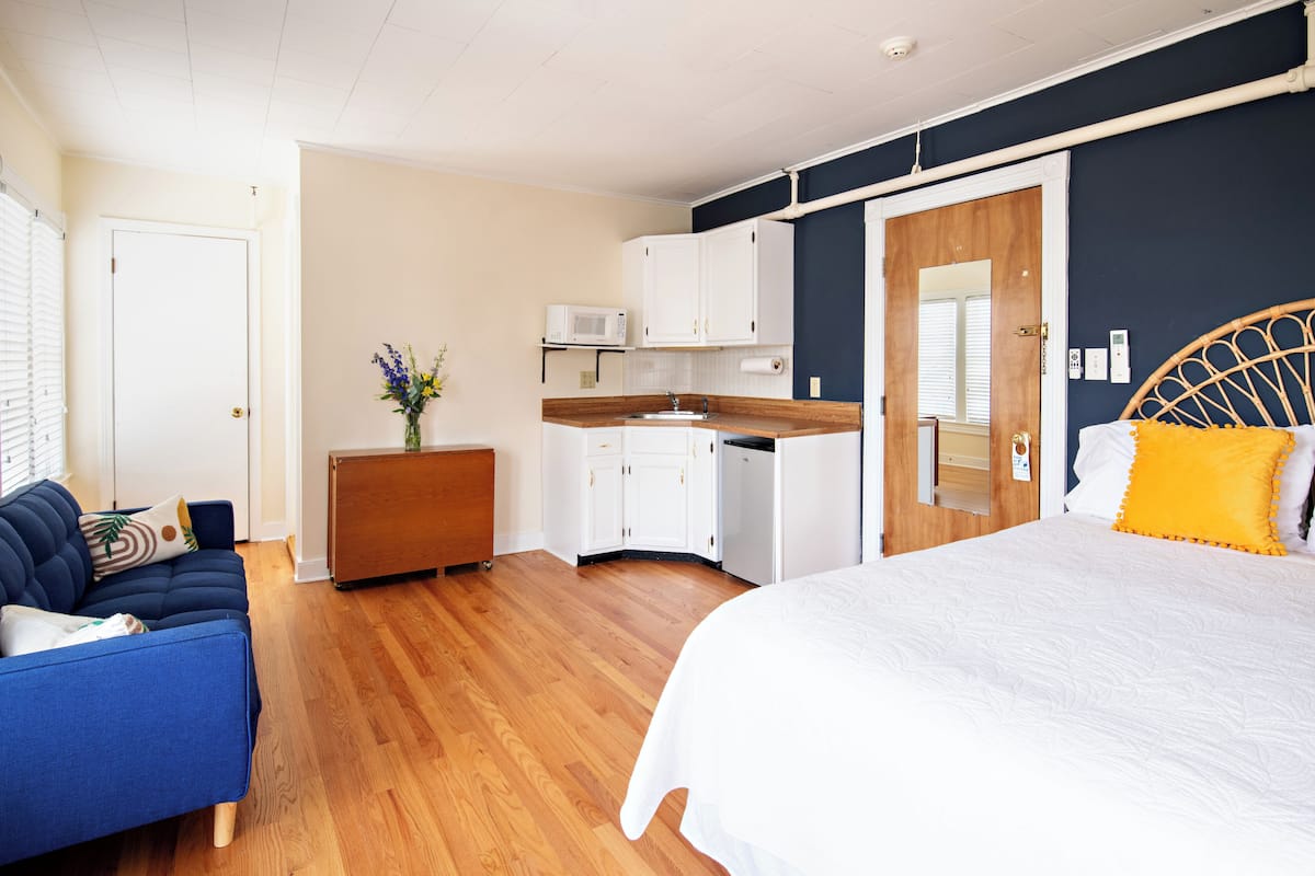 A bedroom with a bed, a sofa, a small kitchenette, and a bathroom door.