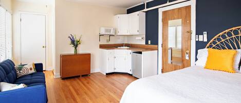 A bedroom with a bed, a sofa, a small kitchenette, and a bathroom door.