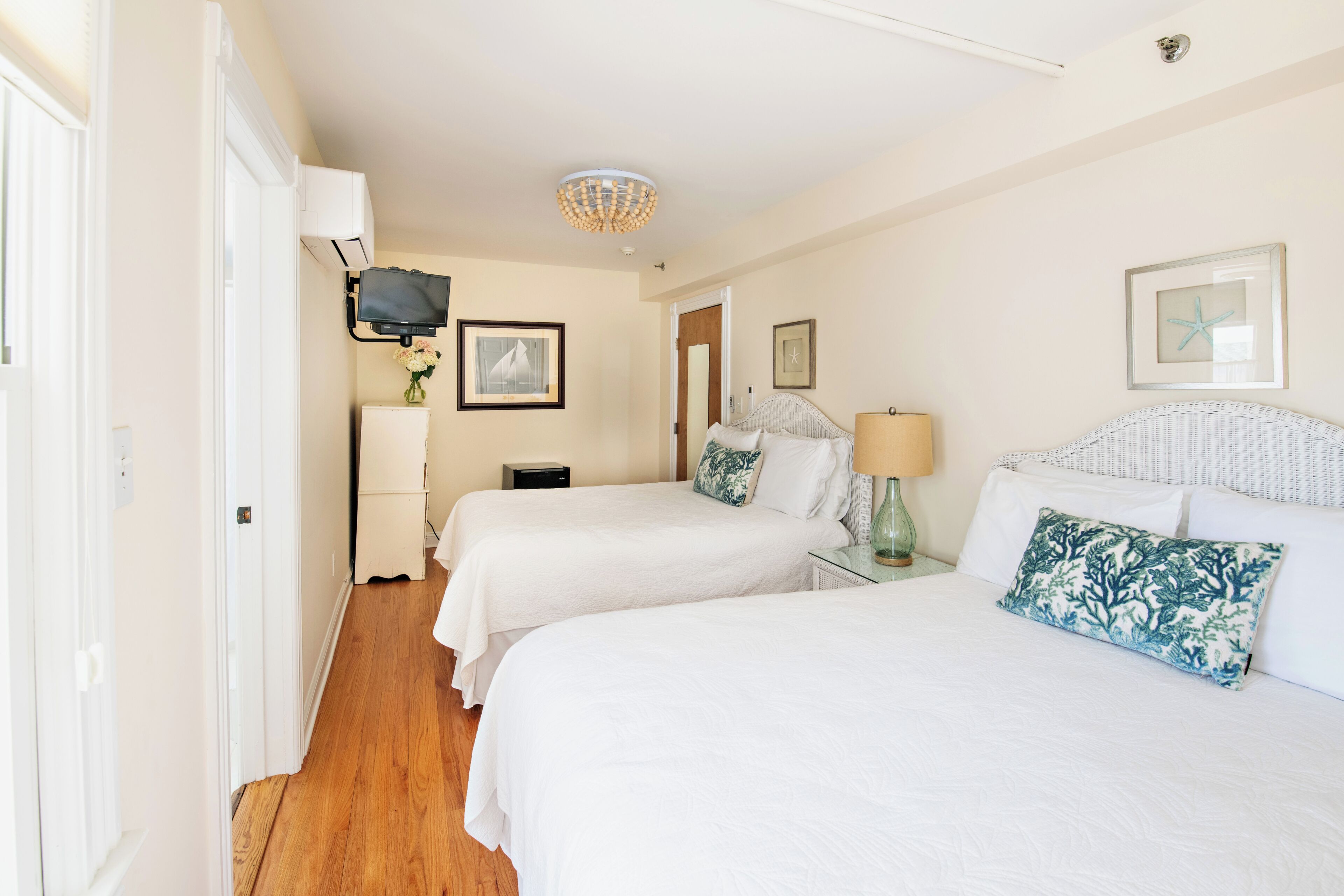 A hotel room with two beds, a television, a ceiling light fixture, and framed pictures on the walls.