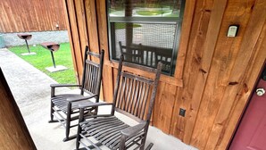 Two wooden rocking chairs on a concrete porch with a wooden wall and a window. - Turkey Trot #73 Cabin in town, walking distance to courthouse square. (Mountain View)