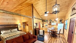 A cozy cabin interior with a wooden ceiling, a sofa, a dining table, and a kitchen area with a refrigerator and microwave. - Turkey Trot #73 Cabin in town, walking distance to courthouse square. (Mountain View)