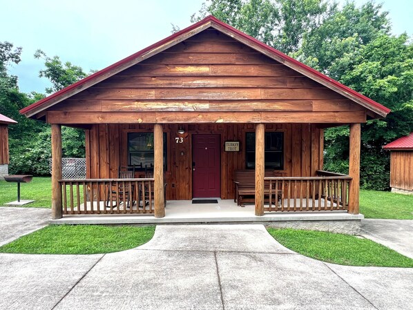 Une cabane en bois avec une porte rouge et le numéro 73, dotée d’un porche avec des bancs et une petite table.