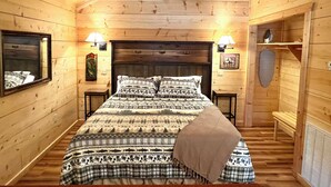 A wooden cabin bedroom with a bed, two bedside lamps, a headboard, a mirror, and a wall-mounted shelf. - Turkey Trot #73 Cabin in town, walking distance to courthouse square. (Mountain View)