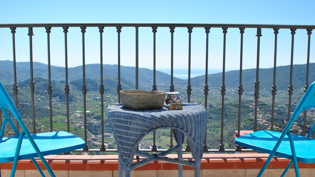 A balcony with a table and chairs, overlooking a mountainous landscape.