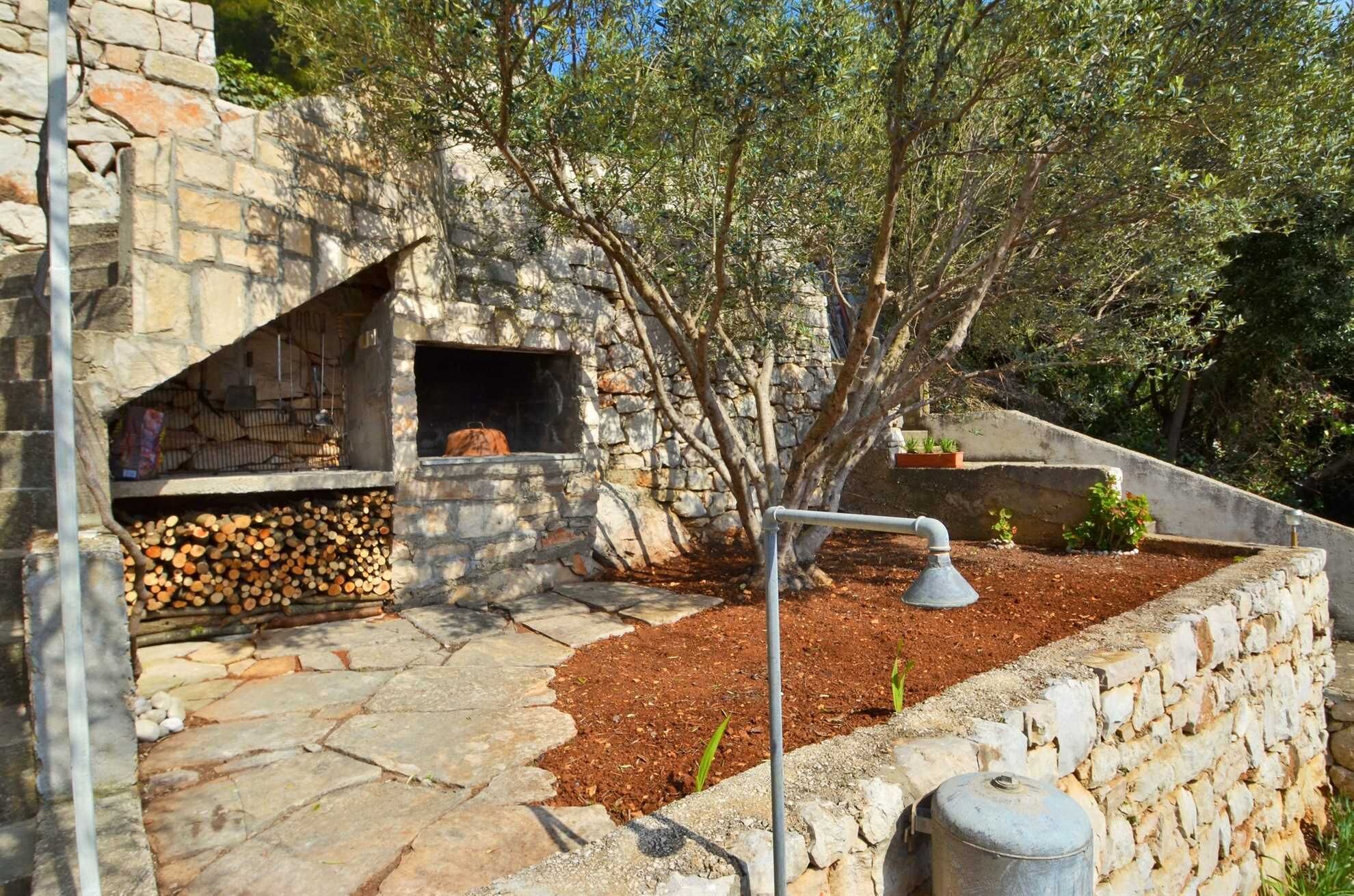A stone-built outdoor cooking area with a wood-fired oven, a metal grill, and a fire pit.