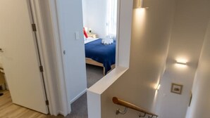 Un escalier avec une rampe, des marches recouvertes de moquette et une vue sur une chambre à coucher avec un lit et des rideaux.