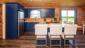 A modern kitchen with blue cabinets, a stainless steel refrigerator, and a large island with four chairs.