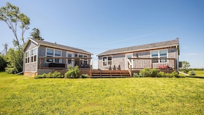 A modern two-story house with large windows and a deck, surrounded by a grassy yard.