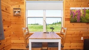 A wooden cabin interior with a dining table, two chairs, a tripod, and a painting of flowers.