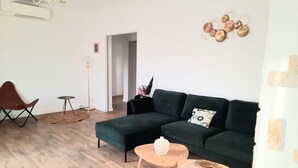A modern living room with a dark green sectional sofa, a small round coffee table, a floor lamp, and a decorative wall piece.