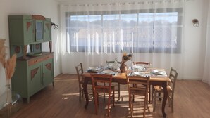 A dining area with a wooden table set for four, a green cabinet, and a window with sheer curtains.