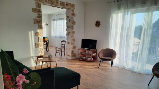 A living room with a sofa, a TV stand, a chair, and a dining area with a table and chairs.