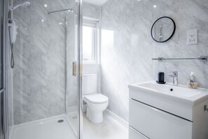 Une salle de bain moderne avec une douche à parois de verre, des toilettes blanches et un meuble-lavabo doté d’un miroir et d’un distributeur de savon.
