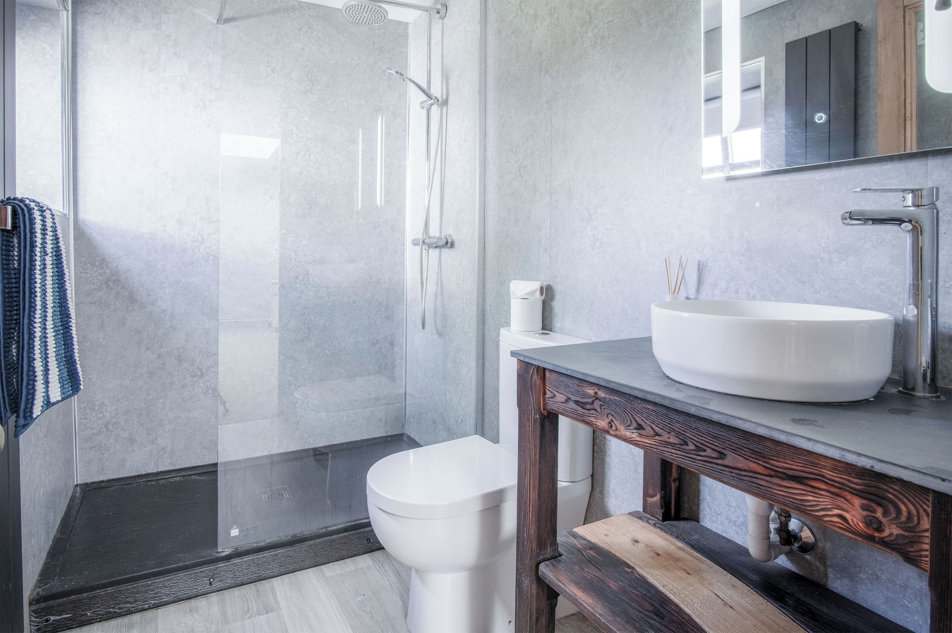 A modern bathroom with a glass shower enclosure, a white toilet, and a wooden vanity with a large sink.