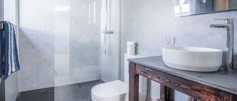 A modern bathroom with a glass shower enclosure, a white toilet, and a wooden vanity with a large sink.